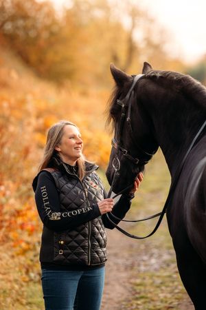 Dark horse and handler share a tender moment on an autumn path surrounded by fall colors.
