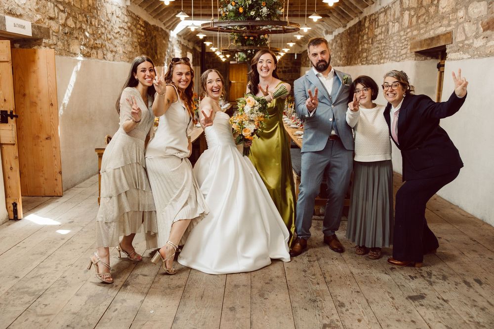 Wedding party poses together in rustic stone venue with wooden floors during celebration sequence.