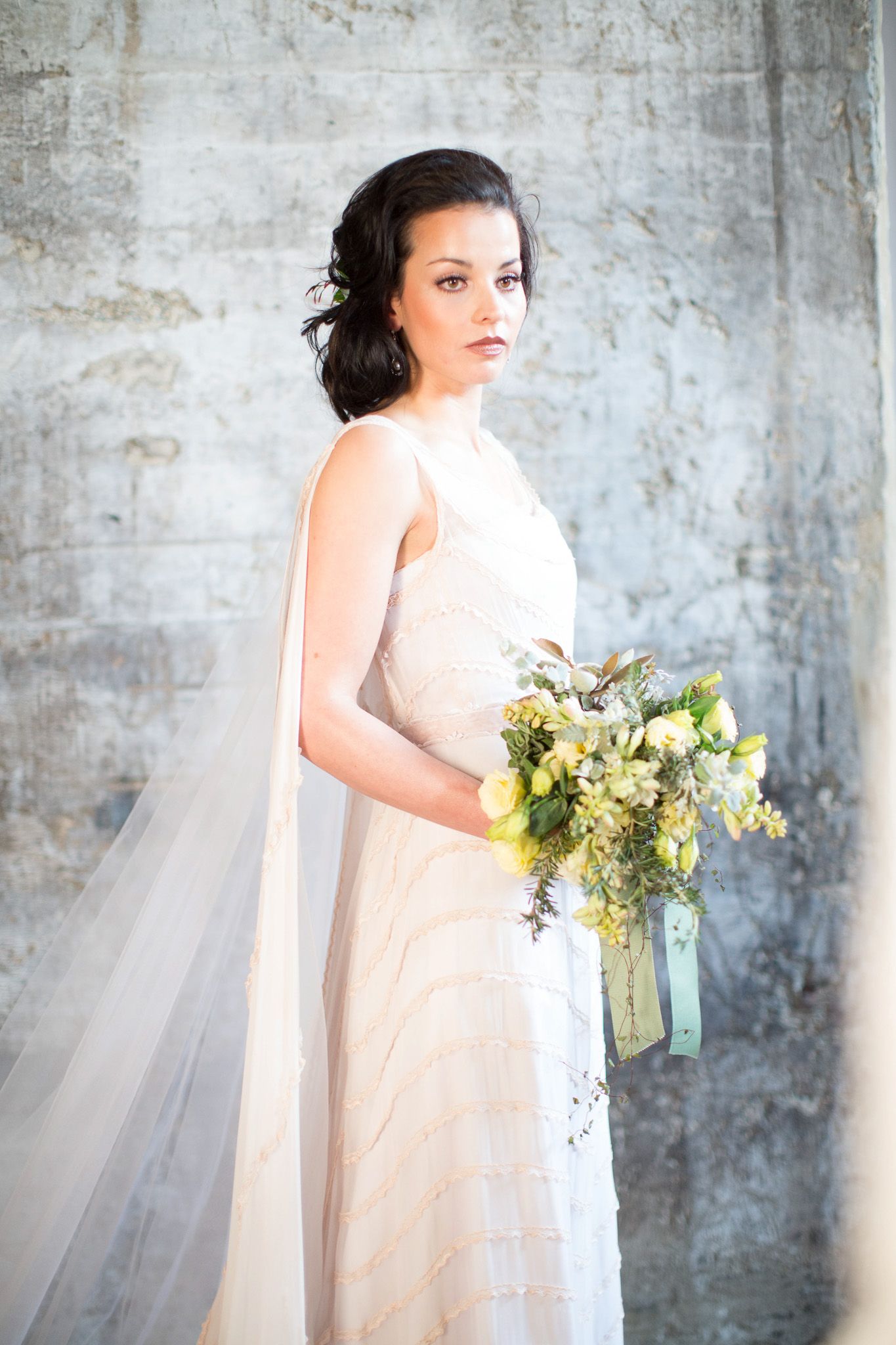 Stunning bride in a flowing champagne gown with veil holding a cascading green and yellow floral bouquet.