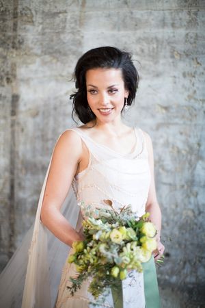 Smiling dark-haired bride in a champagne lace gown holding a green and yellow bouquet with a veil.