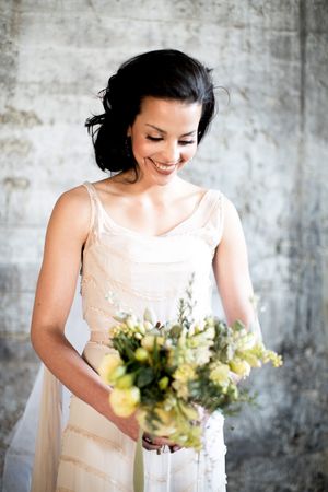Bride in white dress smiling down at green and white wedding bouquet.