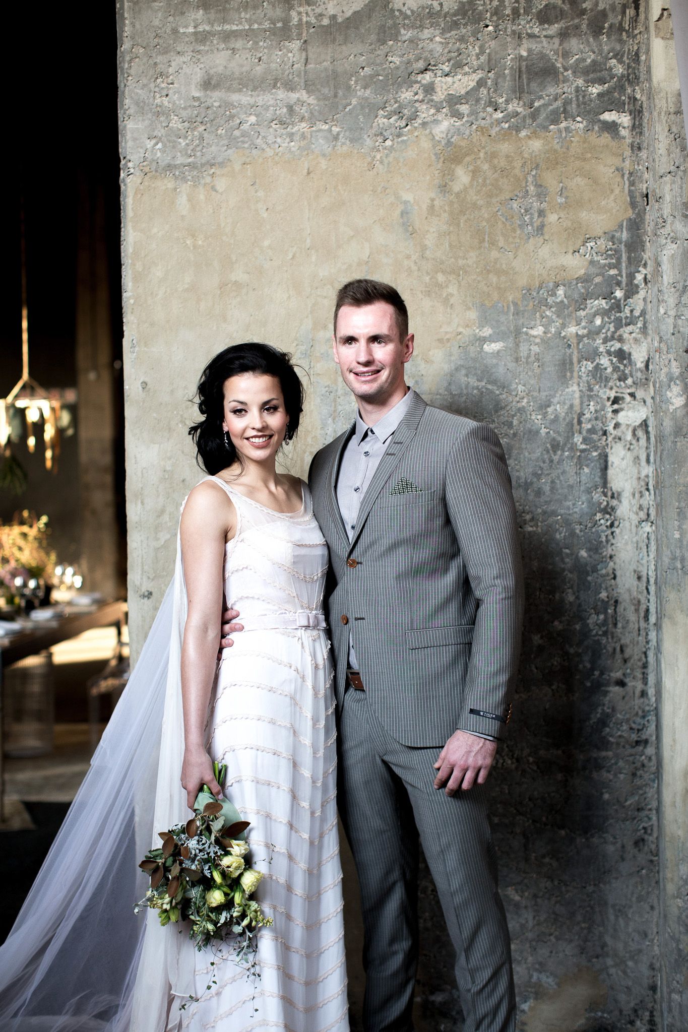 Bride and groom posing together against rustic concrete wall at wedding.
