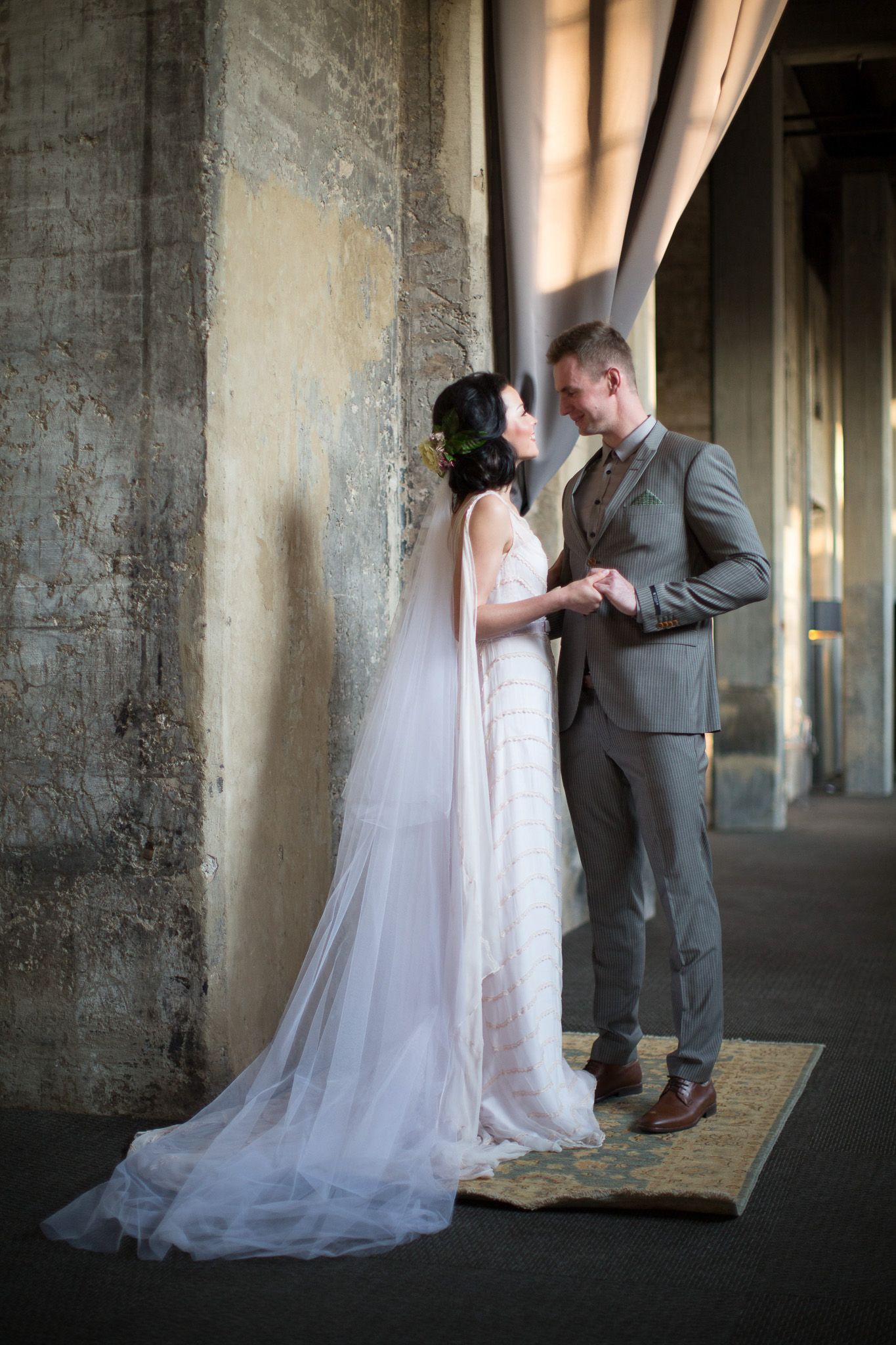 Bride and groom holding hands facing each other in industrial wedding venue.