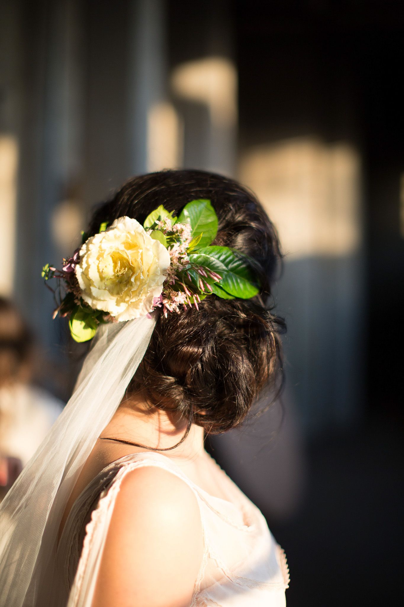 Bride with elegant updo adorned with yellow rose and veil at wedding.