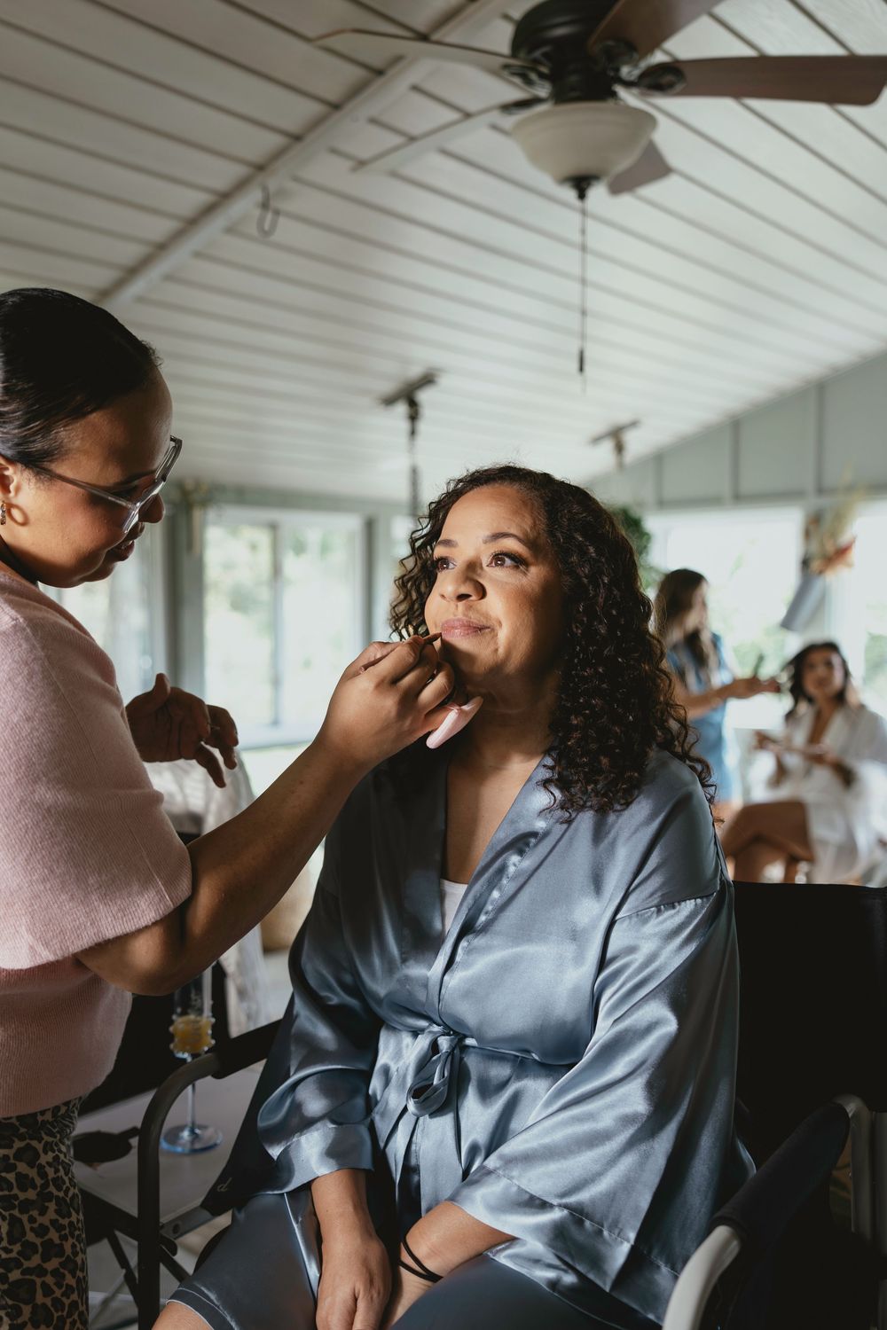 Professional makeup artist applies cosmetics to a client wearing a blue robe during a beauty preparation session.