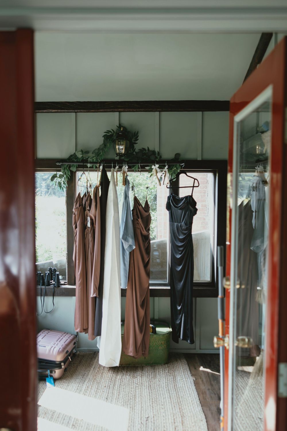 Formal dresses and gowns hanging on clothing racks in a room with wooden floors and large windows.