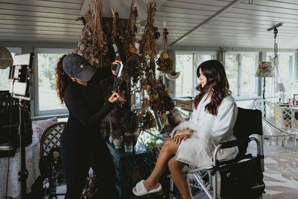 Wedding photographers capture candid moments during a bridal preparation session in a sunlit room.