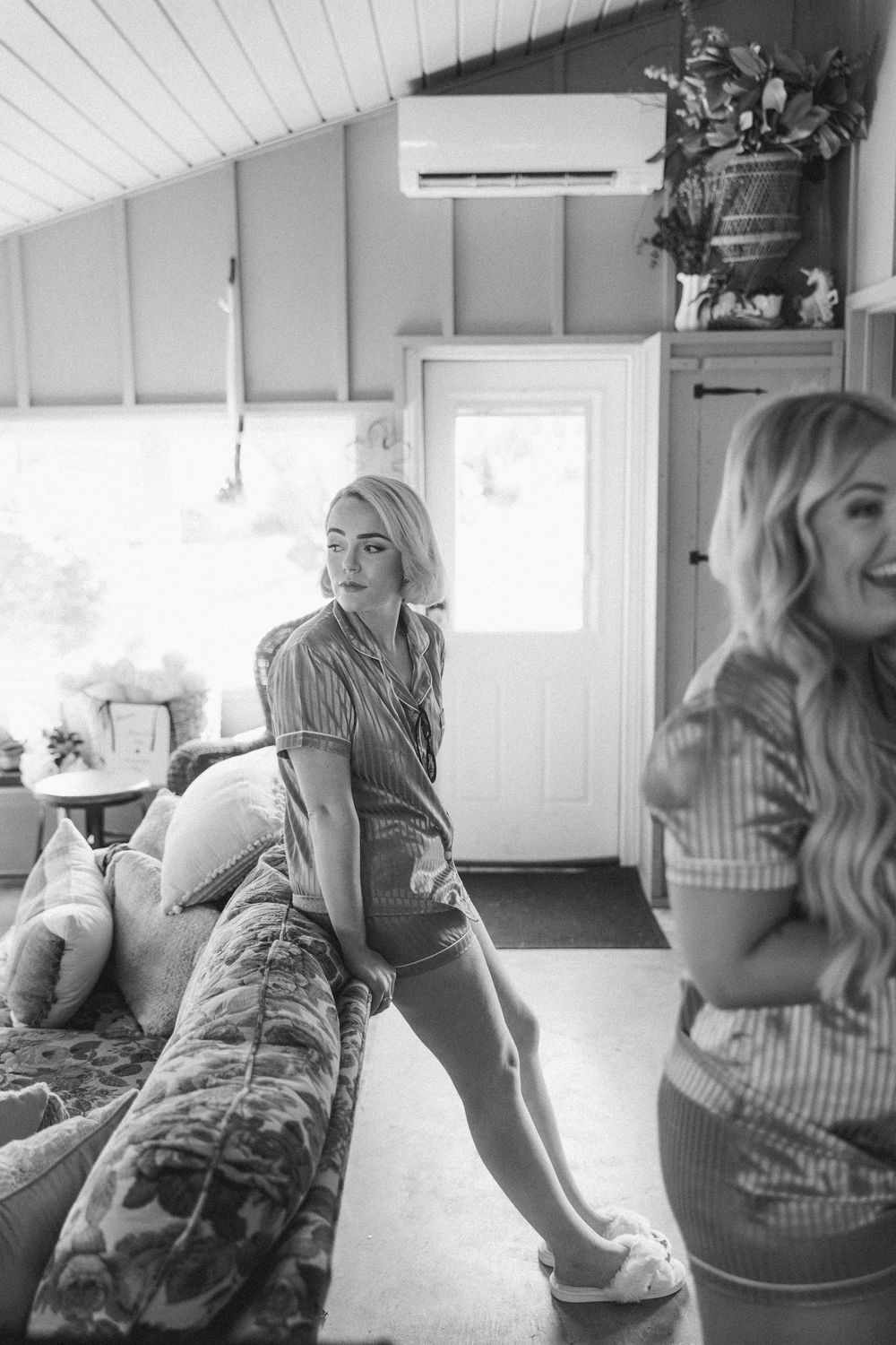 Black and white photo showing two women in casual attire relaxing in a sunlit room with a couch.