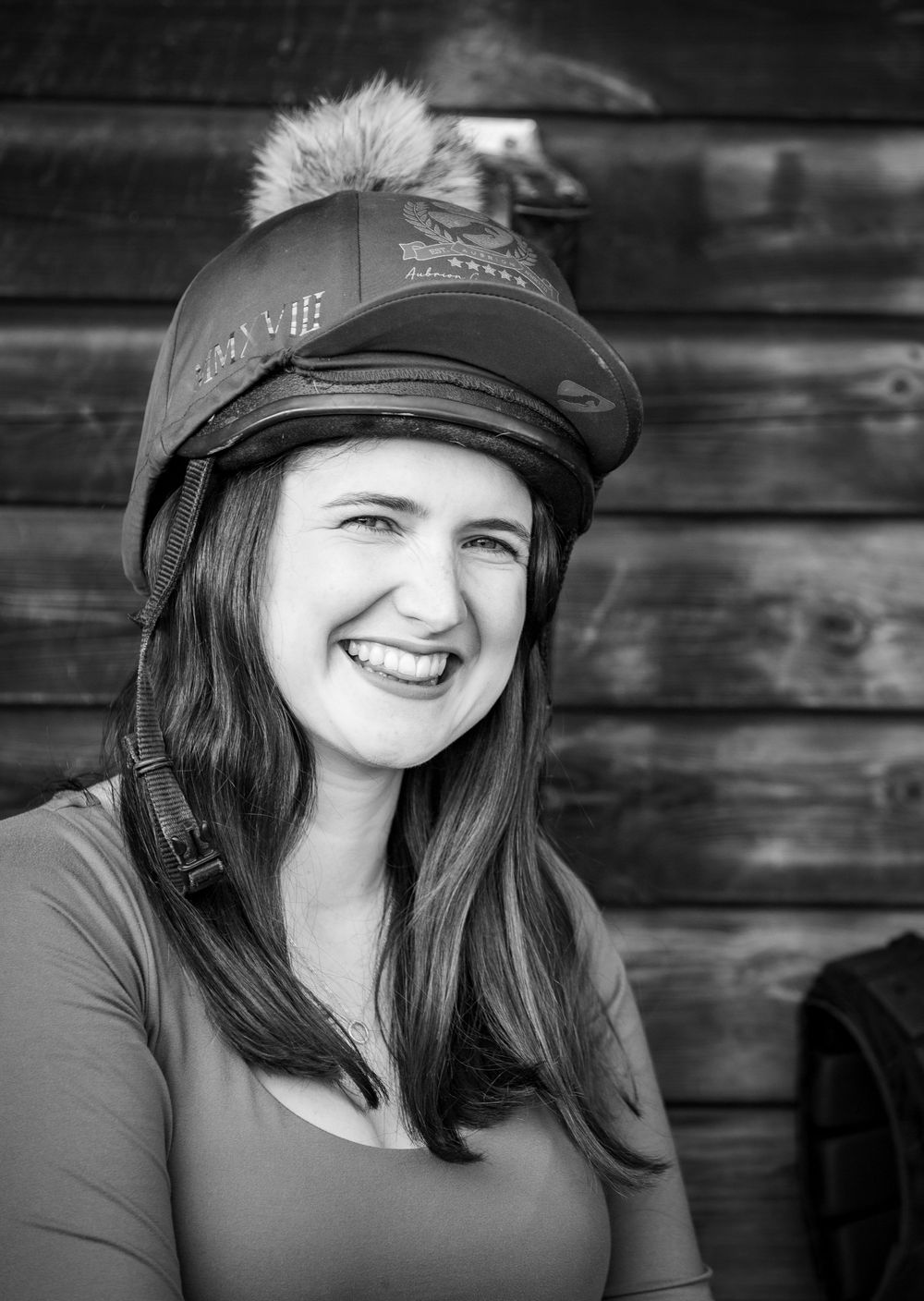 A person wearing a baseball cap and dark shirt smiles in a black and white portrait series against a wooden wall.