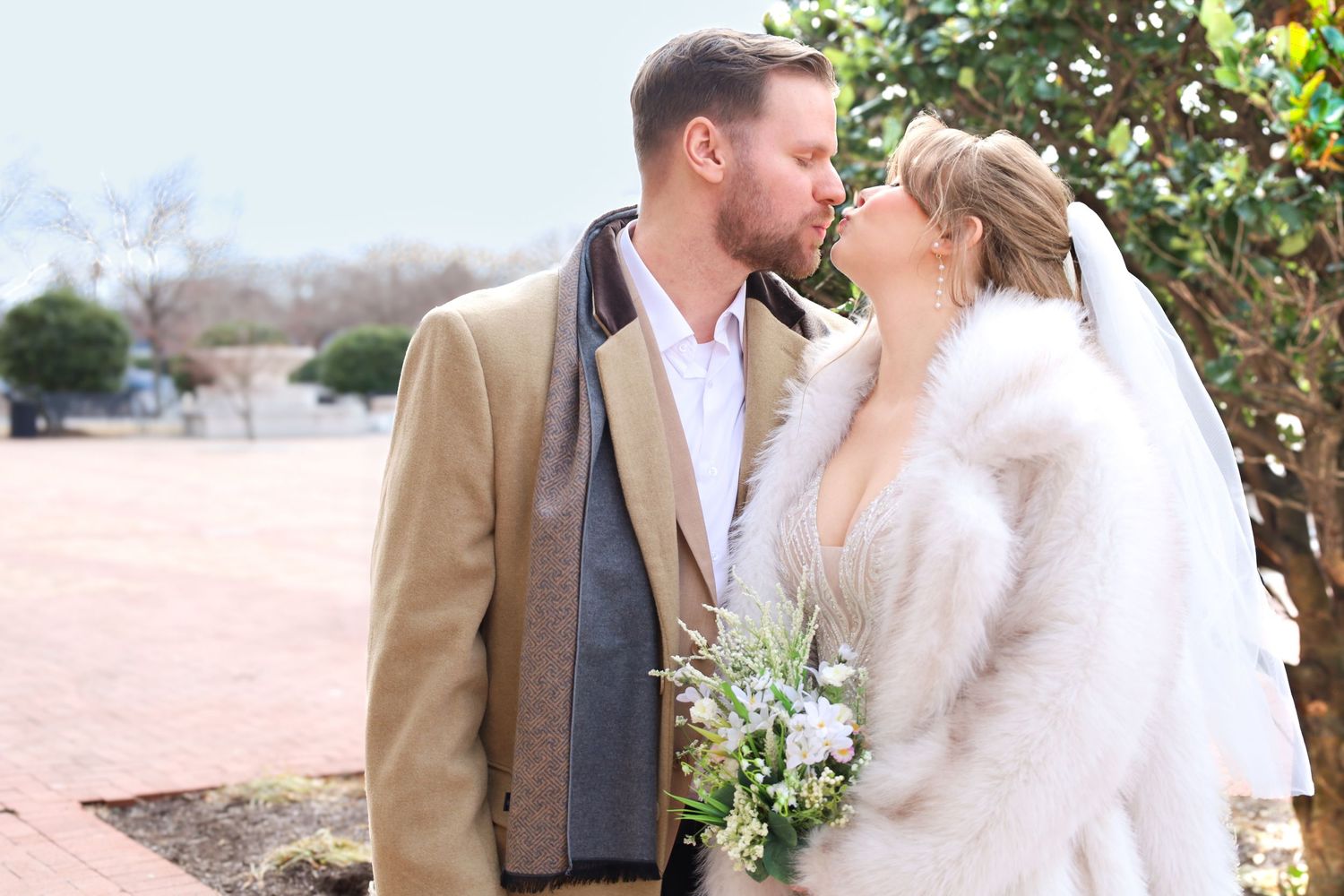 A winter wedding couple in formal attire shares an intimate moment wearing warm coats.