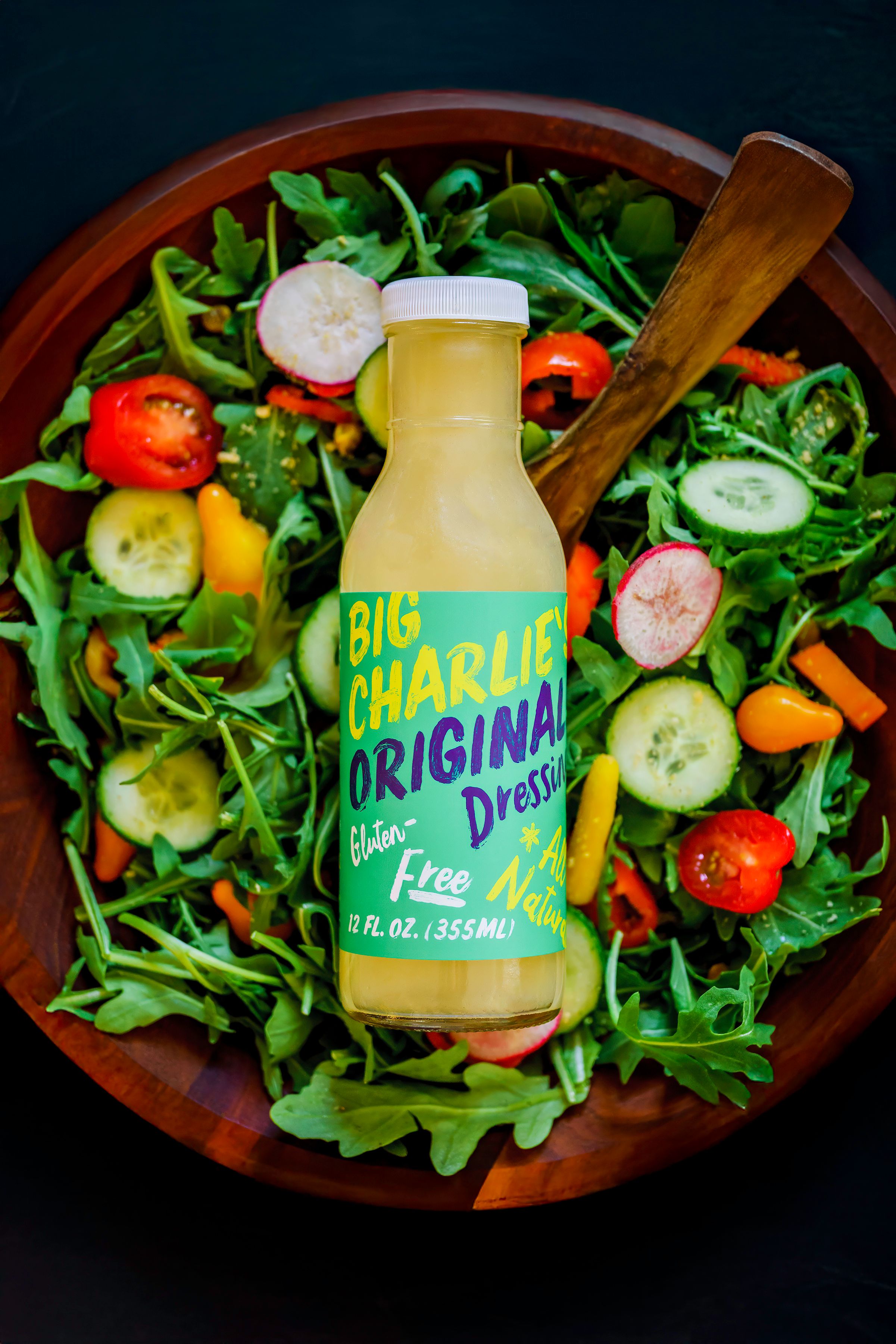 A bottle of Big Charlie's Original dressing nestled in a vibrant salad with fresh tomatoes, cucumbers and arugula greens.