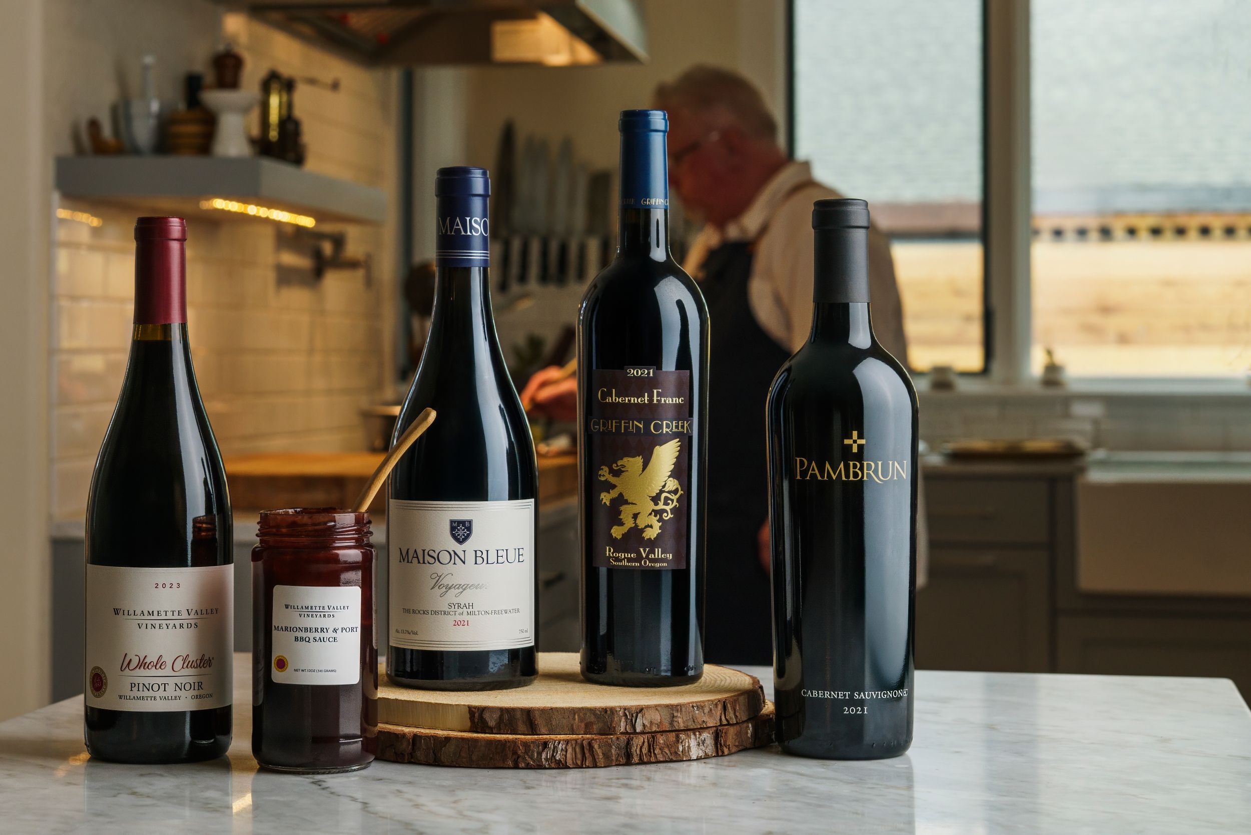 Five bottles of premium red wine displayed on a wooden serving board in a modern kitchen setting.