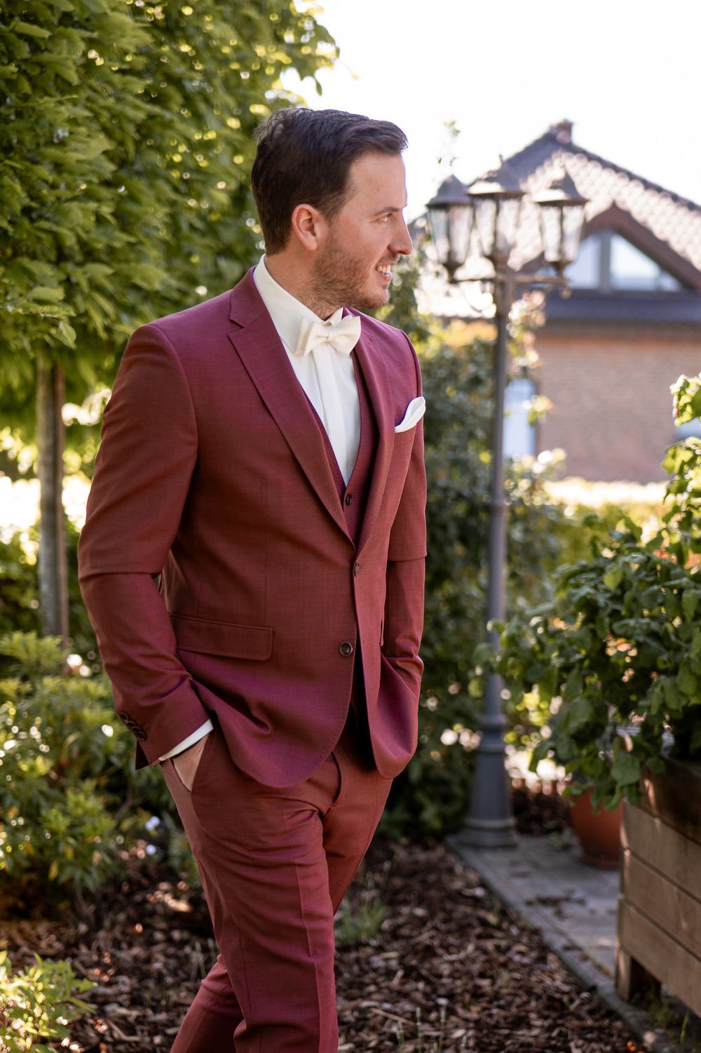 Bräutigam S im bordeauxroten Anzug im herbstlichen Garten. Moderner Hochzeitslook und Männer-Shooting am Niederrhein.