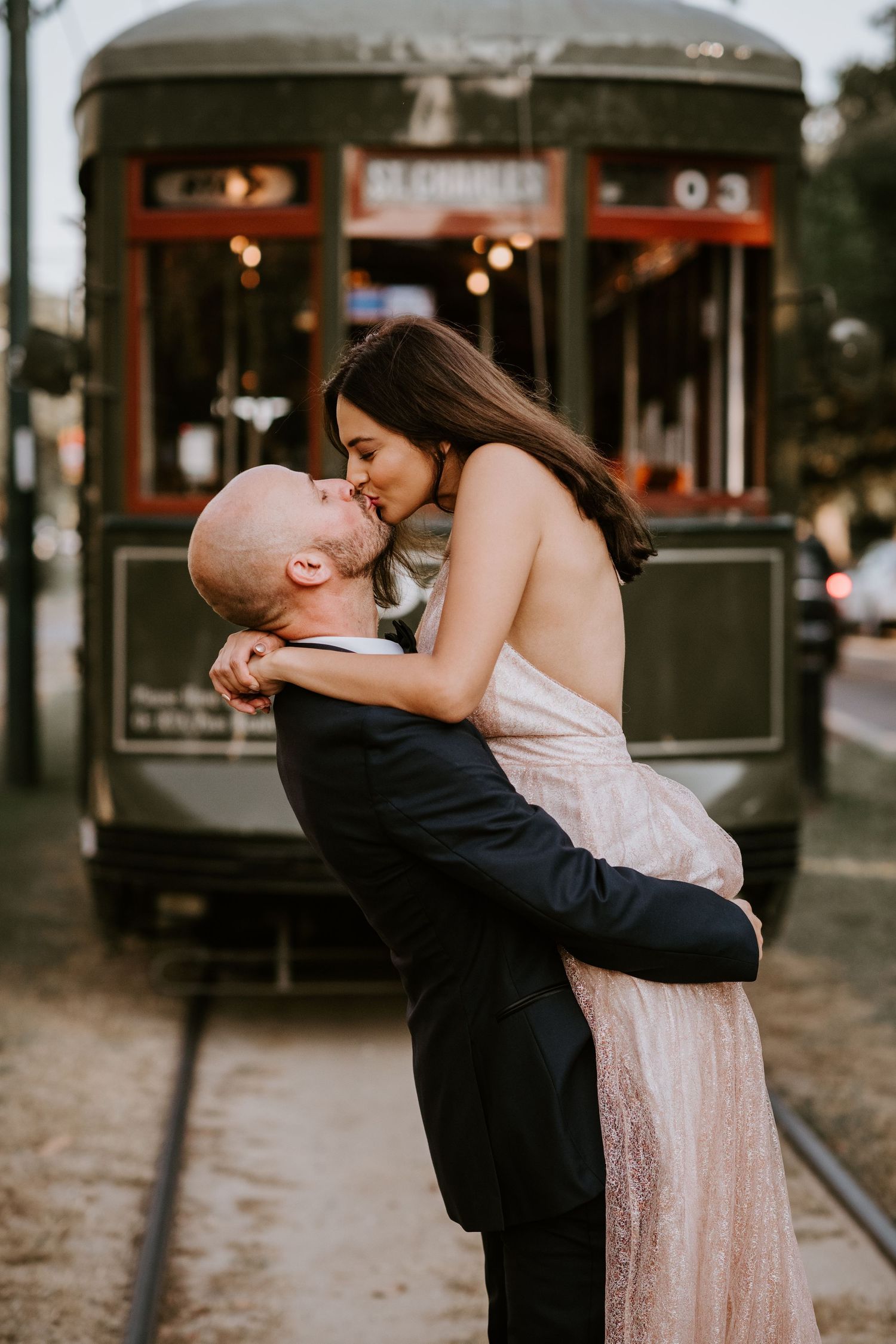 Groom lifts bride for a kiss in front of a vintage New Orleans streetcar at dusk.