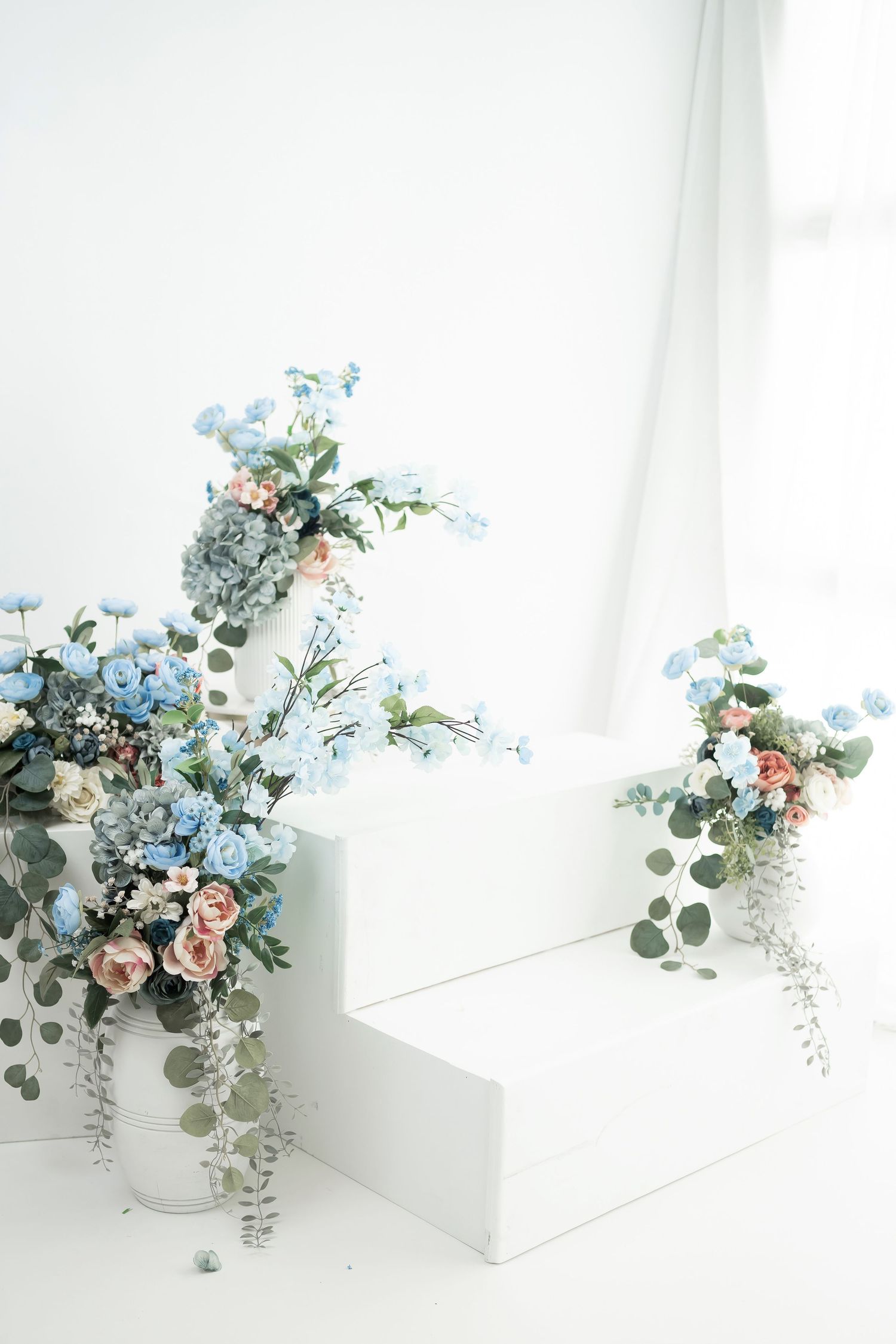 Delicate floral arrangement with pink roses, blue forget-me-nots, and eucalyptus leaves in white ceramic vases.
