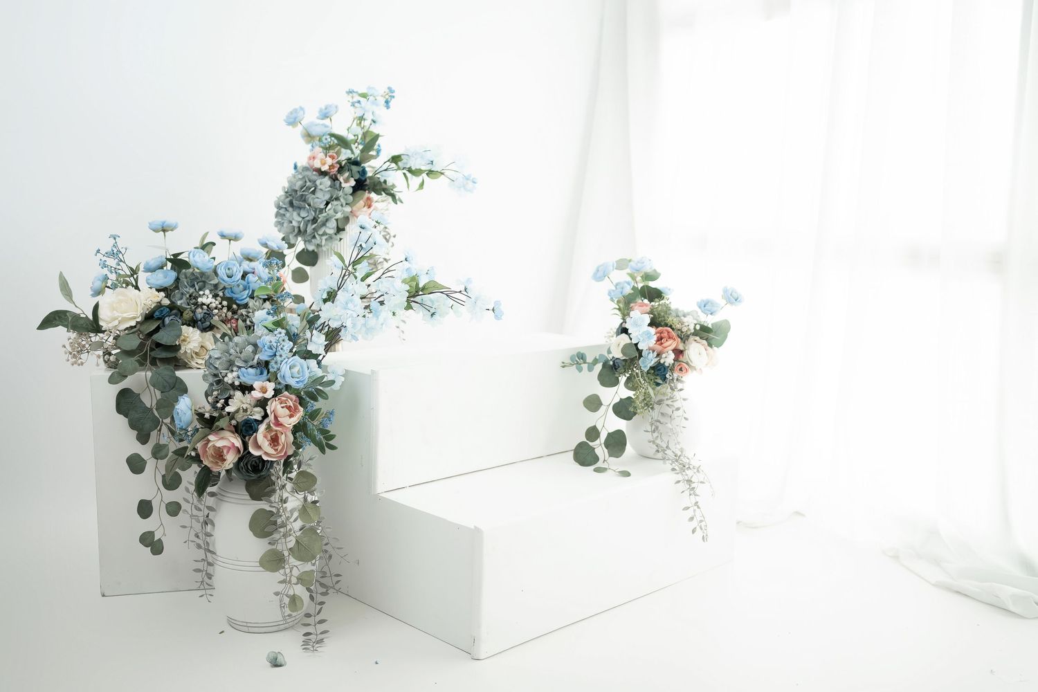 Elegant floral arrangement with blue flowers, pink roses and eucalyptus leaves against a bright white background.