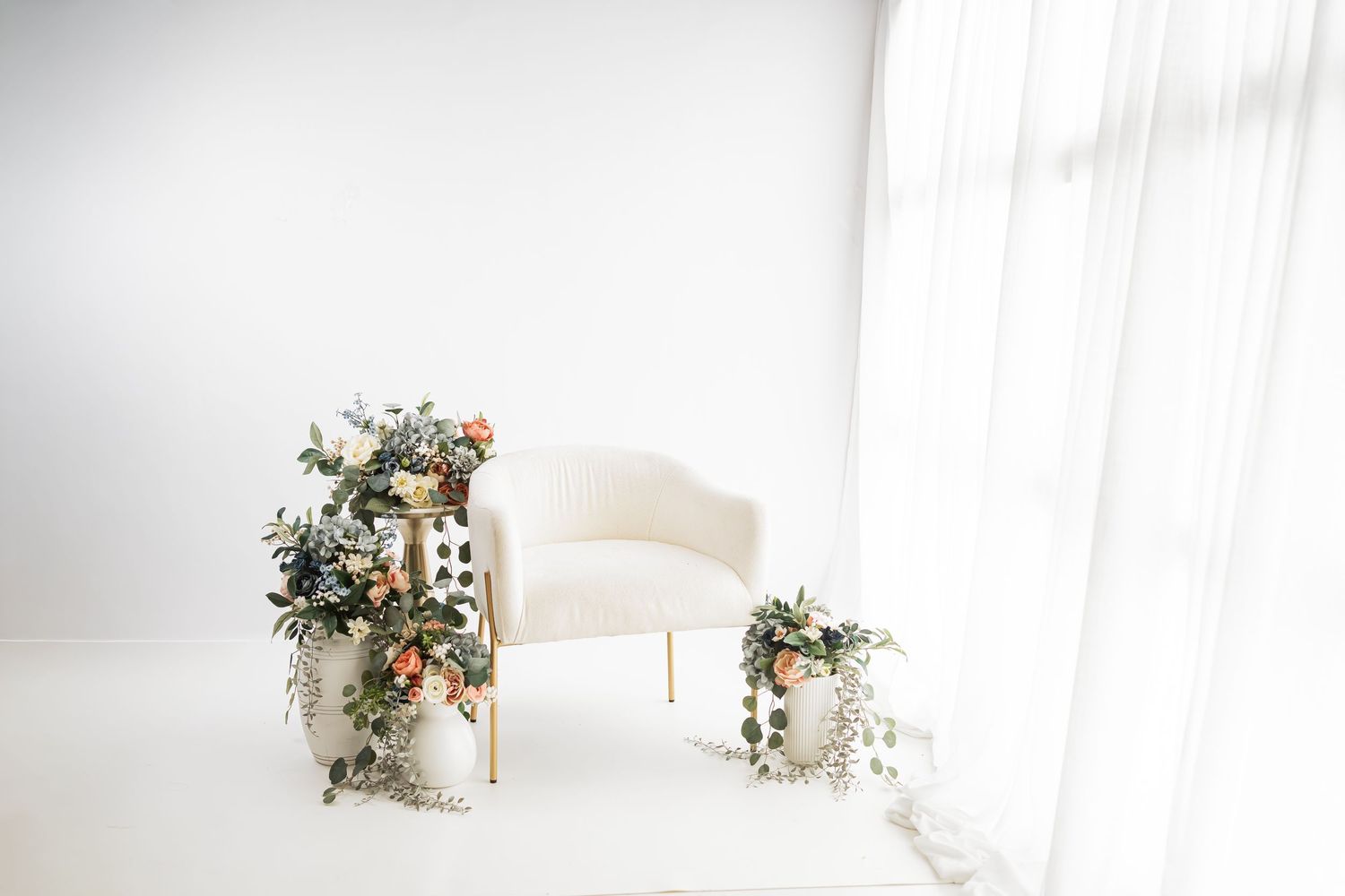 Minimalist white room with floral arrangements and natural light streaming through windows.