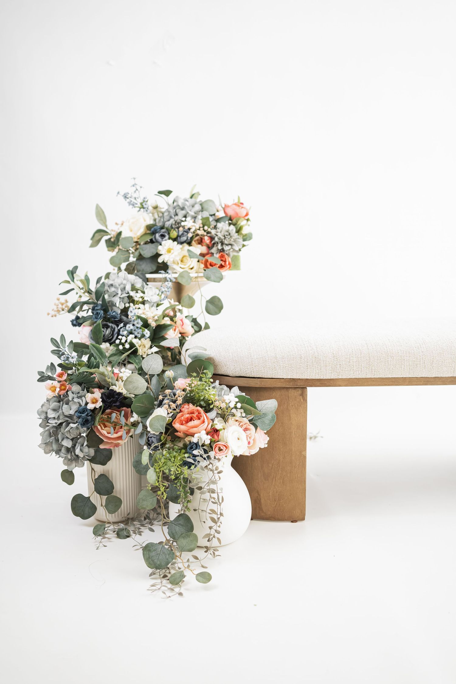 A rustic wooden bench adorned with a lush floral arrangement featuring eucalyptus leaves and peach-colored blooms.