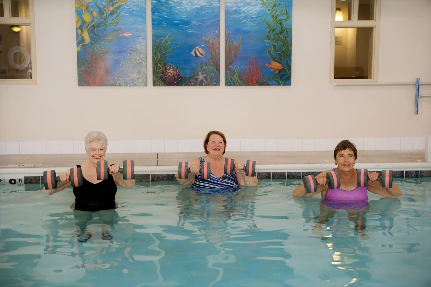 Three female senior citizens exercising in a pool with dumbbells