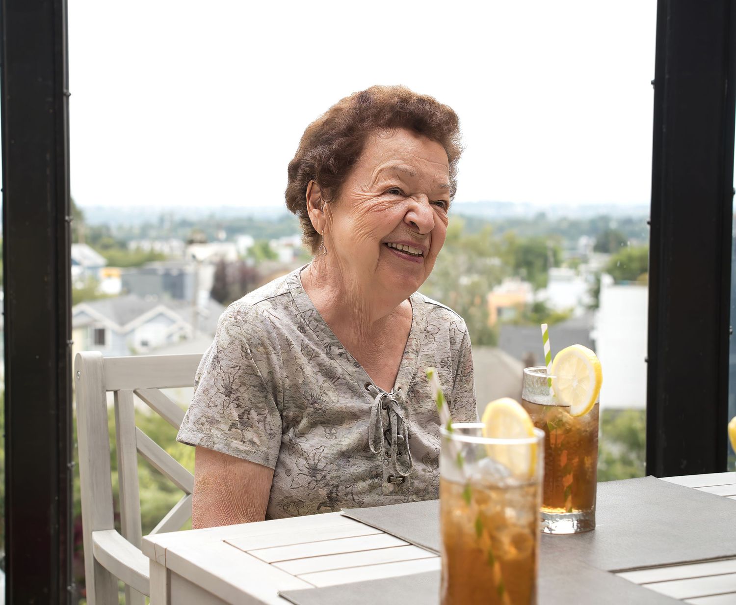 Elderly woman smiling while sitting at a table with ice tea