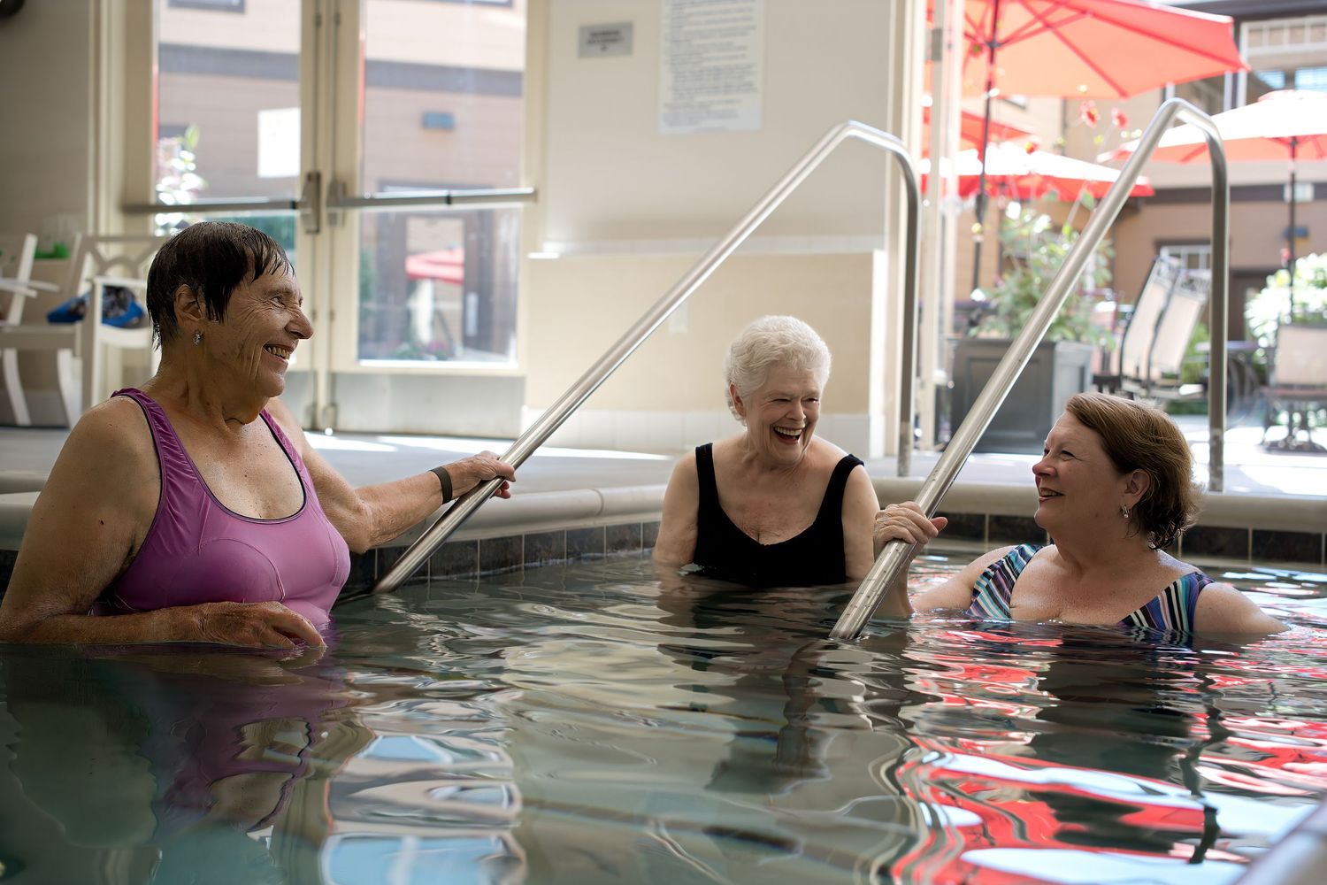 Three female senior citizens standing in a swimming pool having a fun conversation.