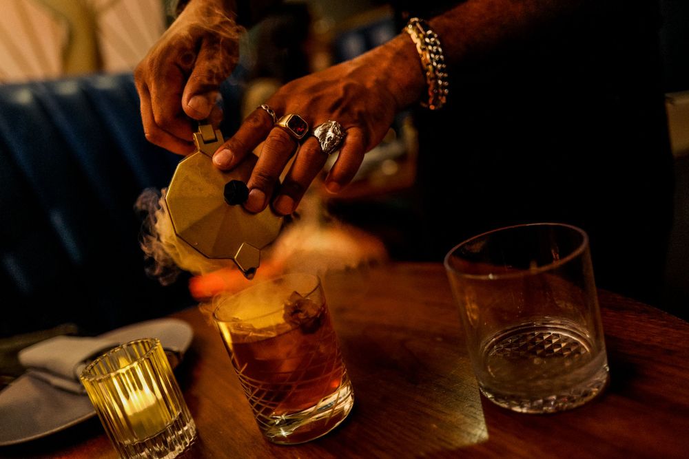 Hands pouring cocktail drink at dimly lit bar with glassware.