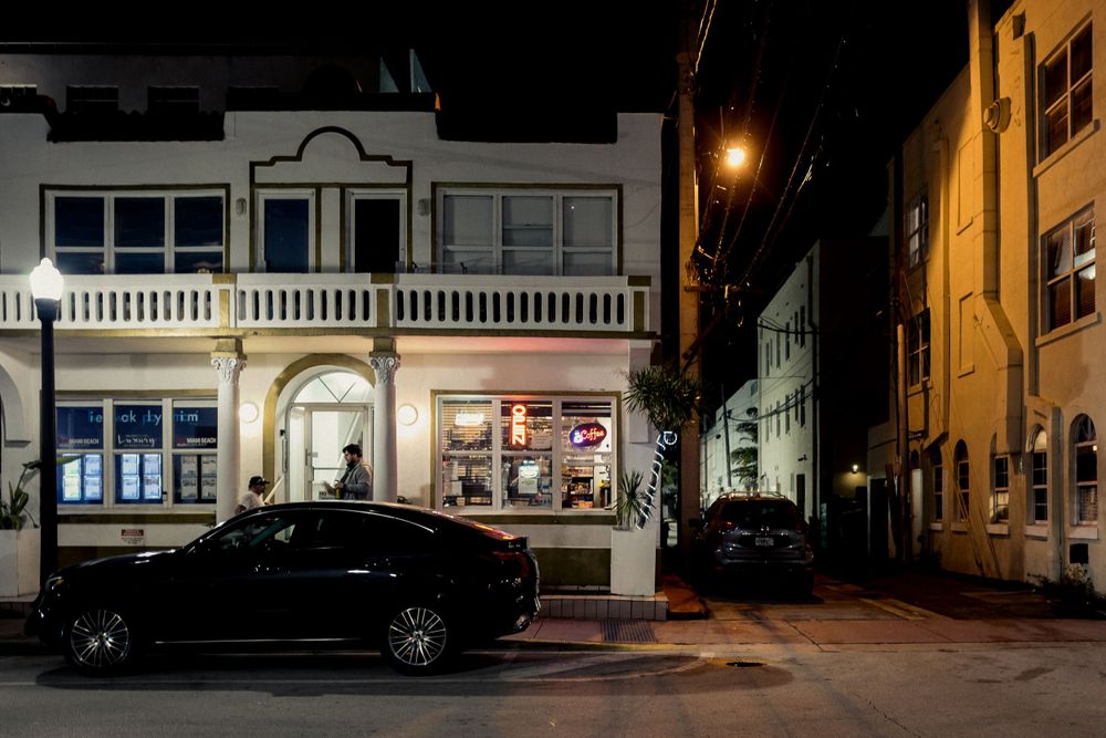 Night view of illuminated vintage storefront with parked cars on quiet street.