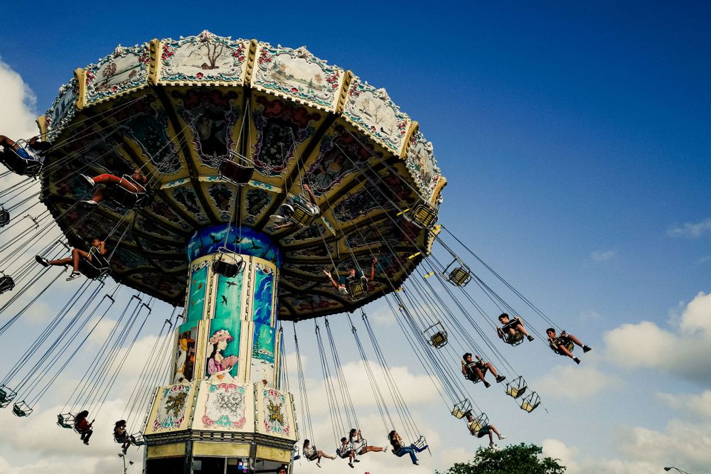 Vintage carousel swing ride spinning against bright blue sky during daytime.