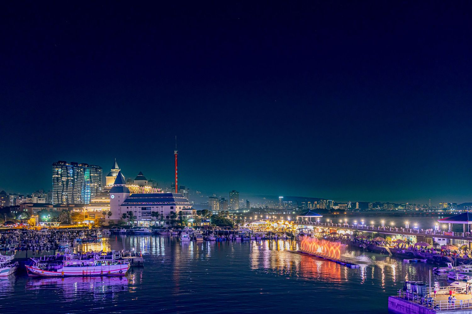 Night cityscape panorama with colorful lights reflecting on calm harbor waters.