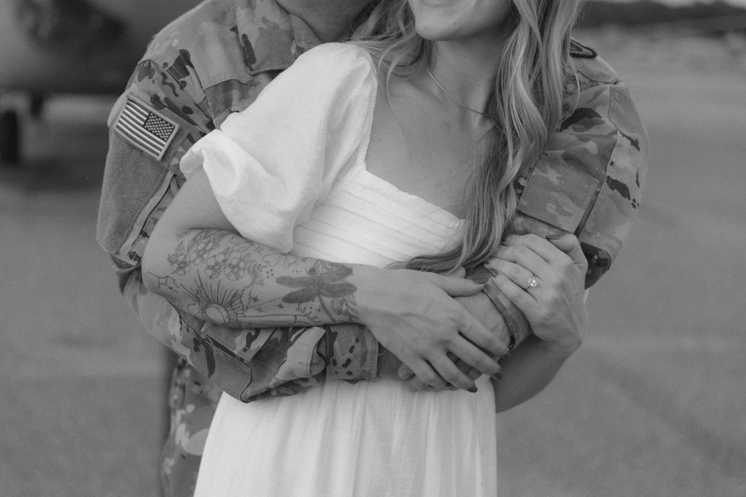 A close-up black and white photo of a couple embracing on a military base.