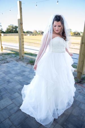 A bride in a flowing white gown twirling on an outdoor patio with wooden posts.