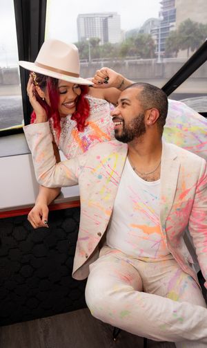 A couple in matching white and pink splatter-painted outfits poses together on a boat.