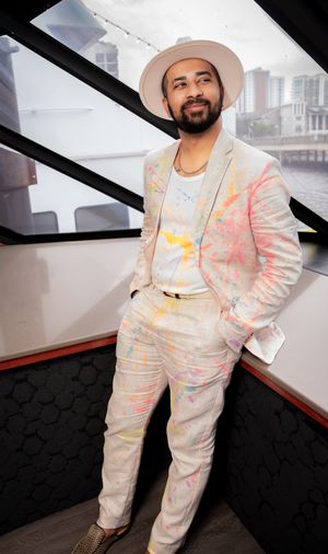 Wedding guest in a colorful splatter-patterned white suit poses in a modern interior space.