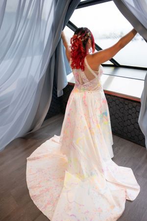 Wedding dress with colorful paint splatters and flowing white fabric photographed in interior setting.