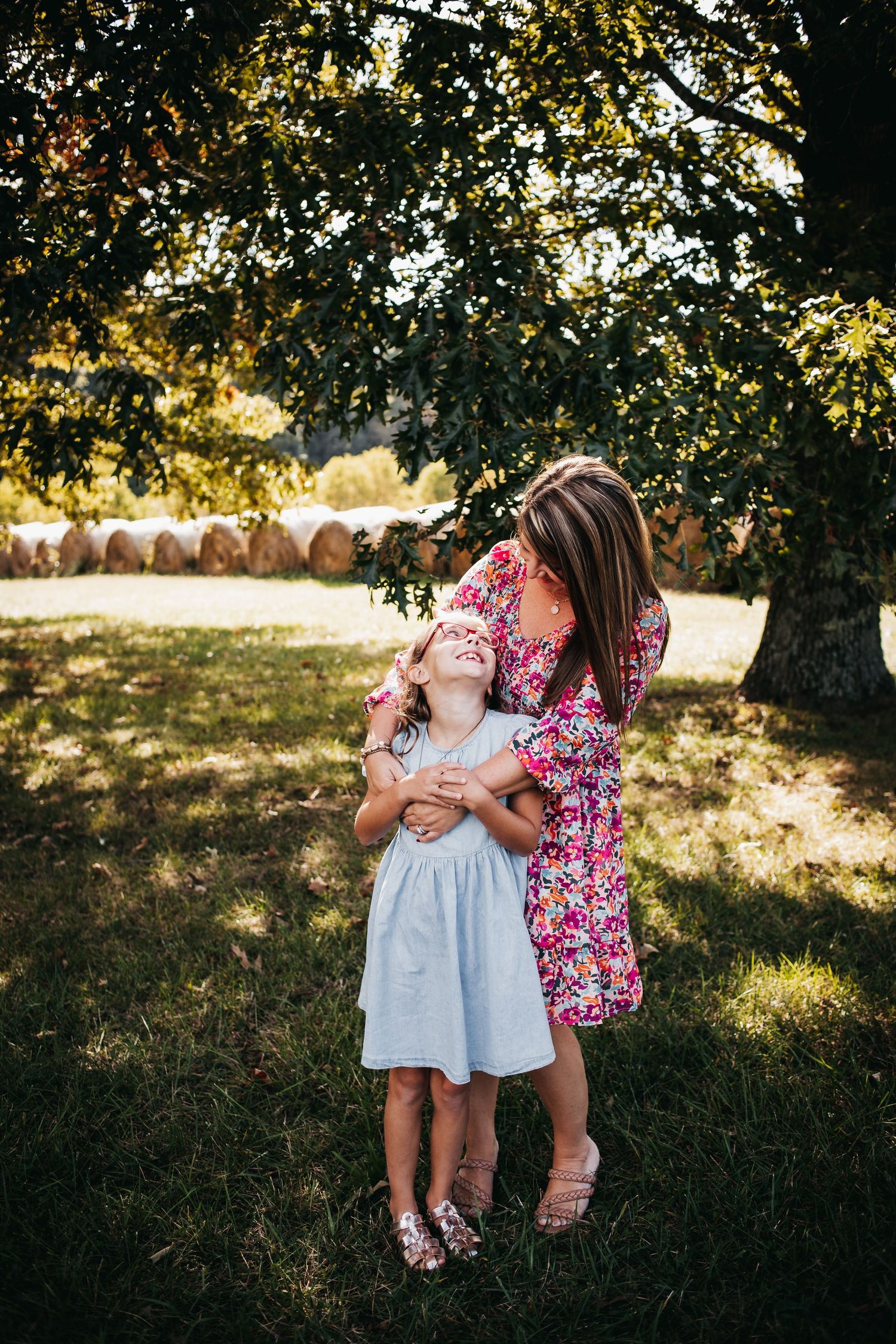 Lindsay embracing her daughter from behind under a shaded tree.