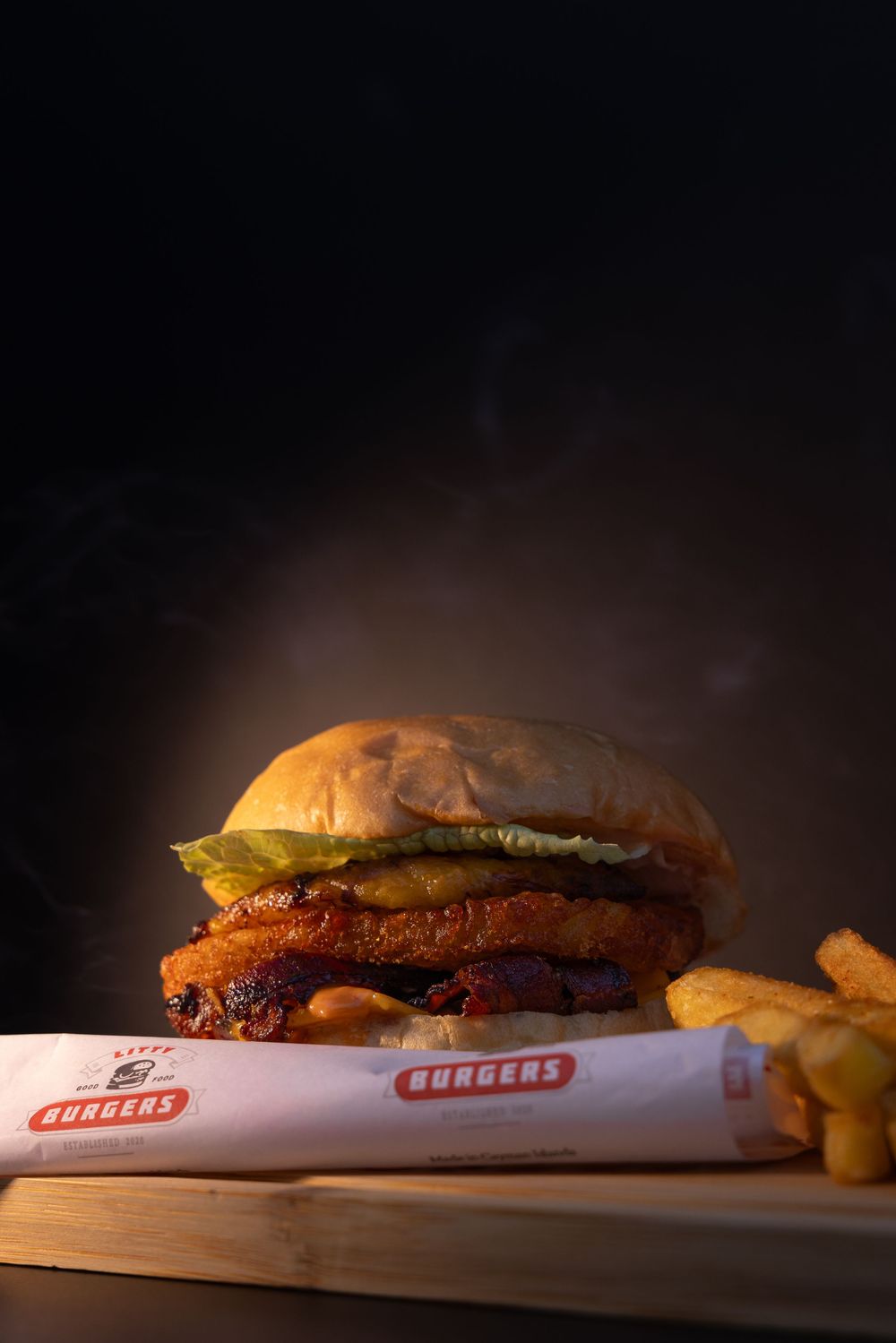 Gourmet burgers with melted cheese and toppings on branded paper wrapping in dramatic lighting.