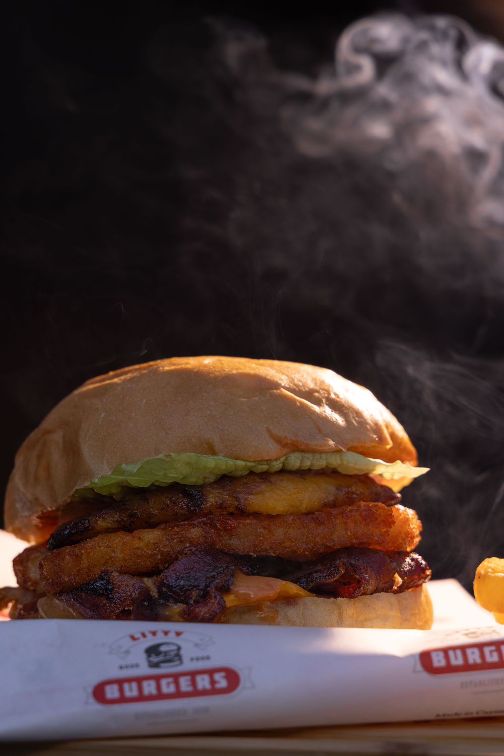 Close-up of steaming hot burgers with fresh toppings on branded restaurant paper.