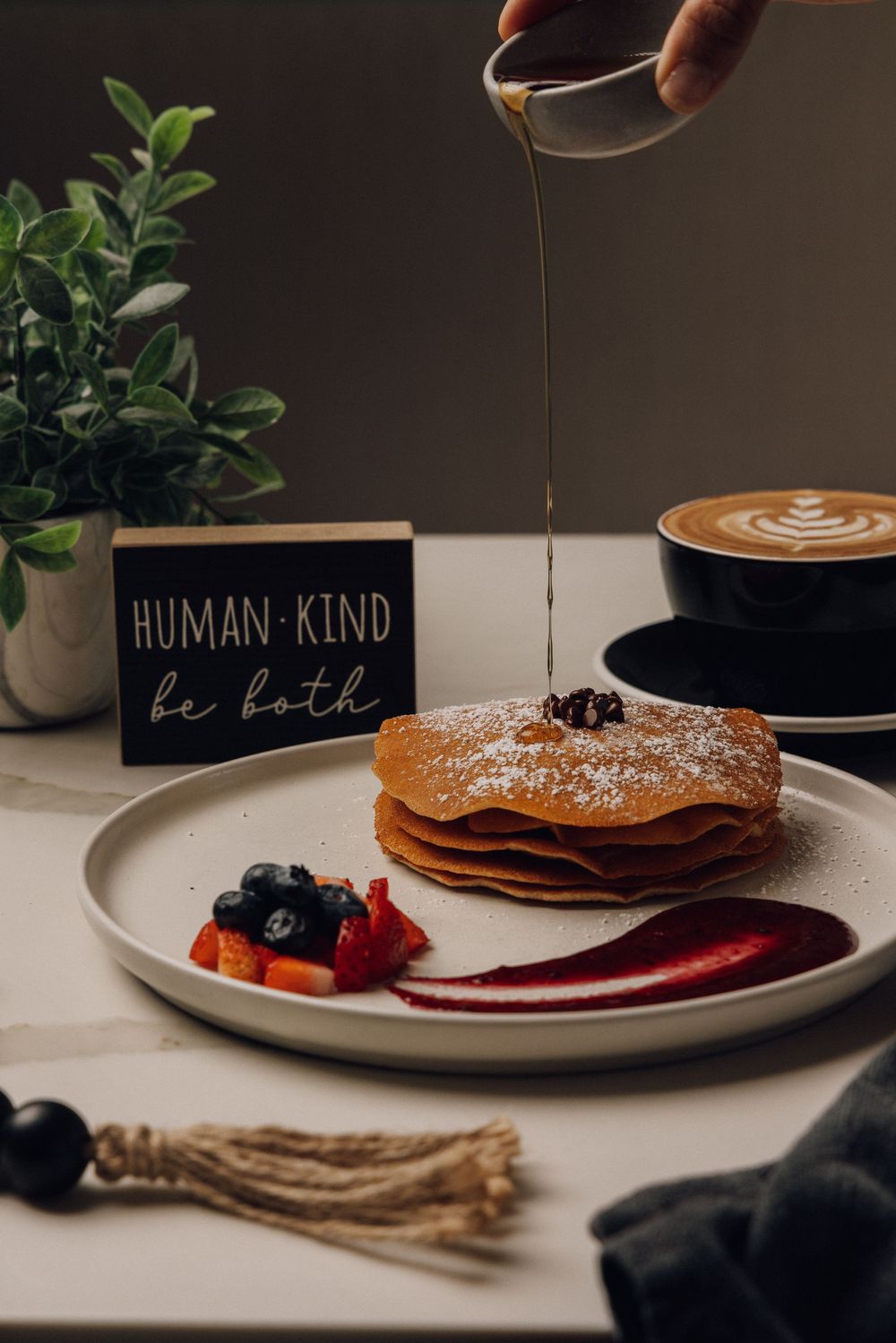 Pancakes and coffee being served on minimalist plates with decorative signs in the background.