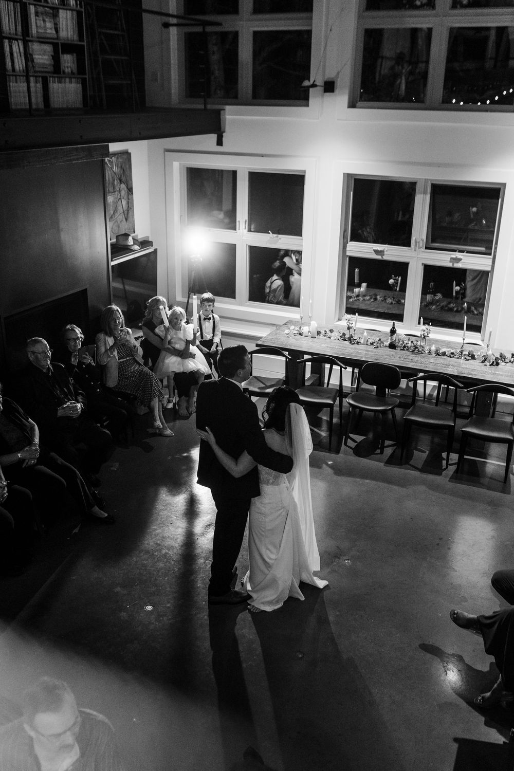 Wedding guests dance together on a dark dance floor illuminated by soft lighting during an evening reception celebration.