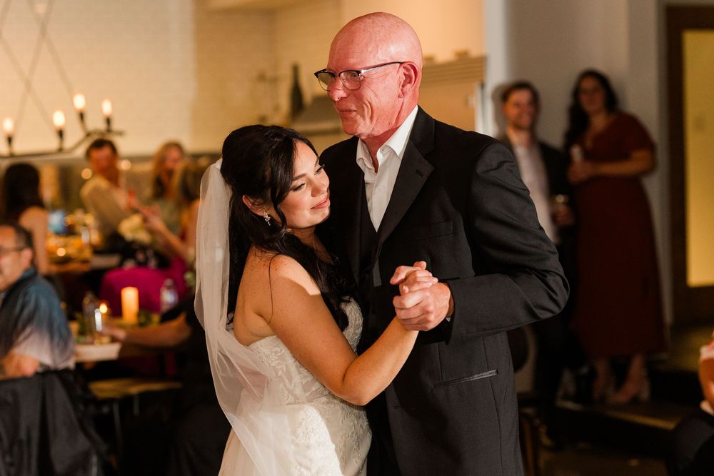 A couple shares an intimate dance moment during their wedding reception in a warmly lit indoor venue.