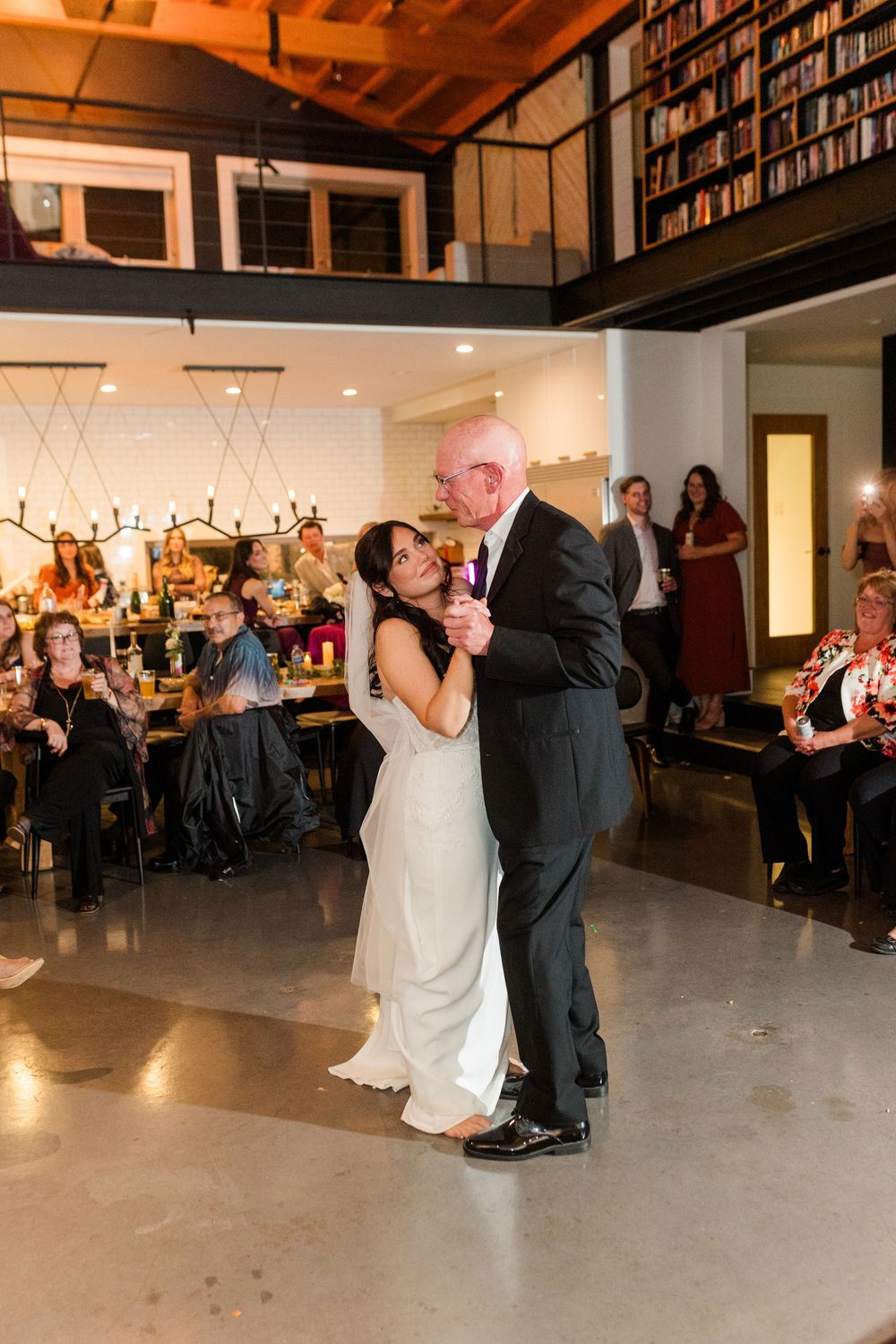 Wedding couple sharing their first dance in a modern venue with bookshelves and warm lighting.