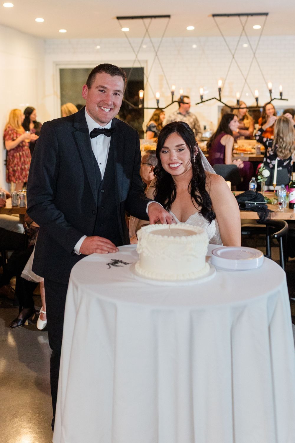 Wedding couple shares a joyful moment while cutting their white wedding cake at an elegant indoor reception venue.