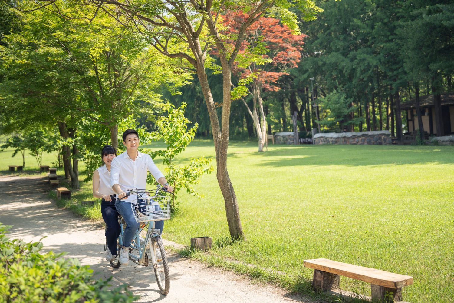 People walking along a scenic park path surrounded by lush green trees and colorful autumn foliage.