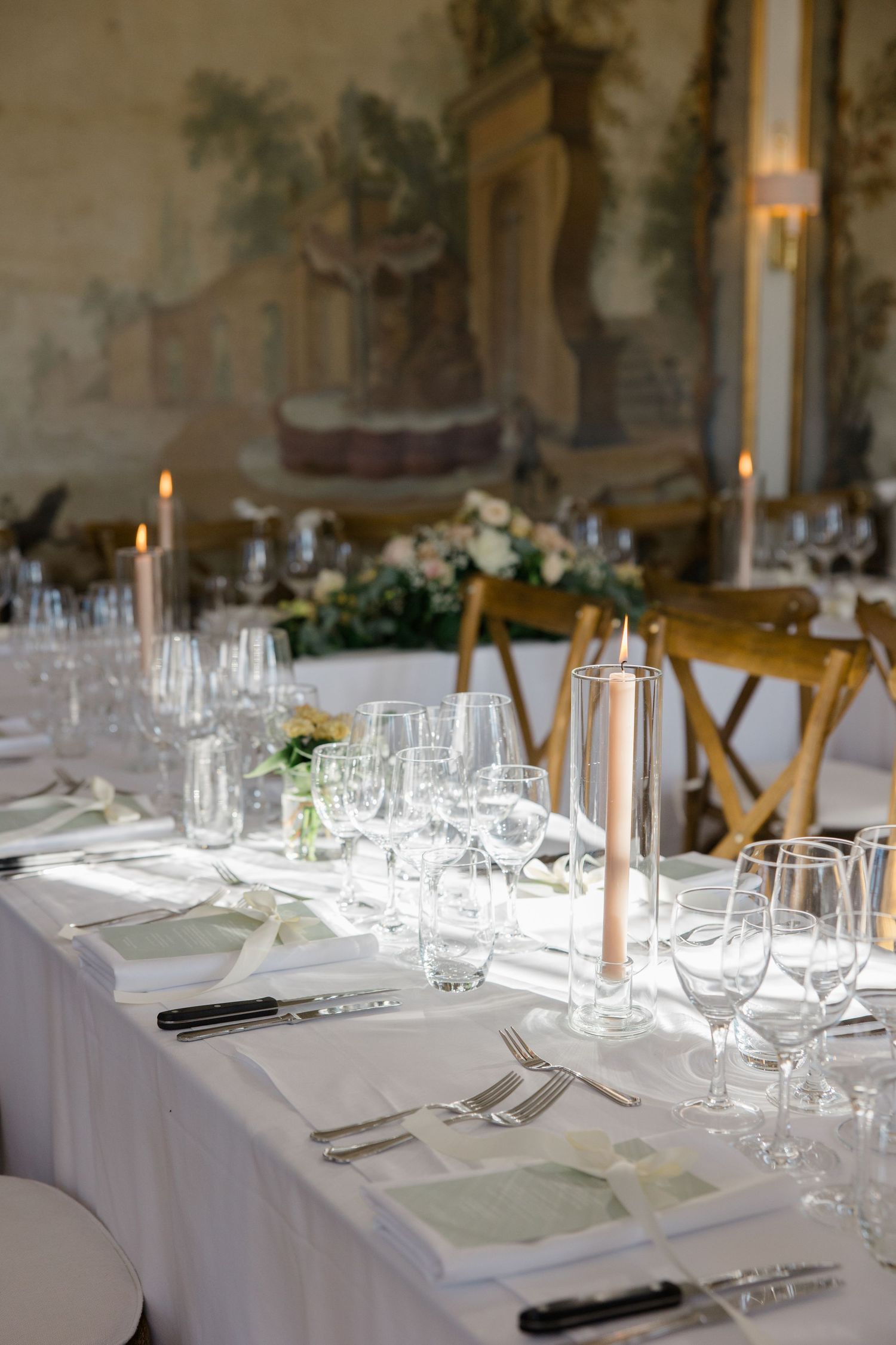 Elegant wedding reception room with crystal chandelier and white-covered chairs.
