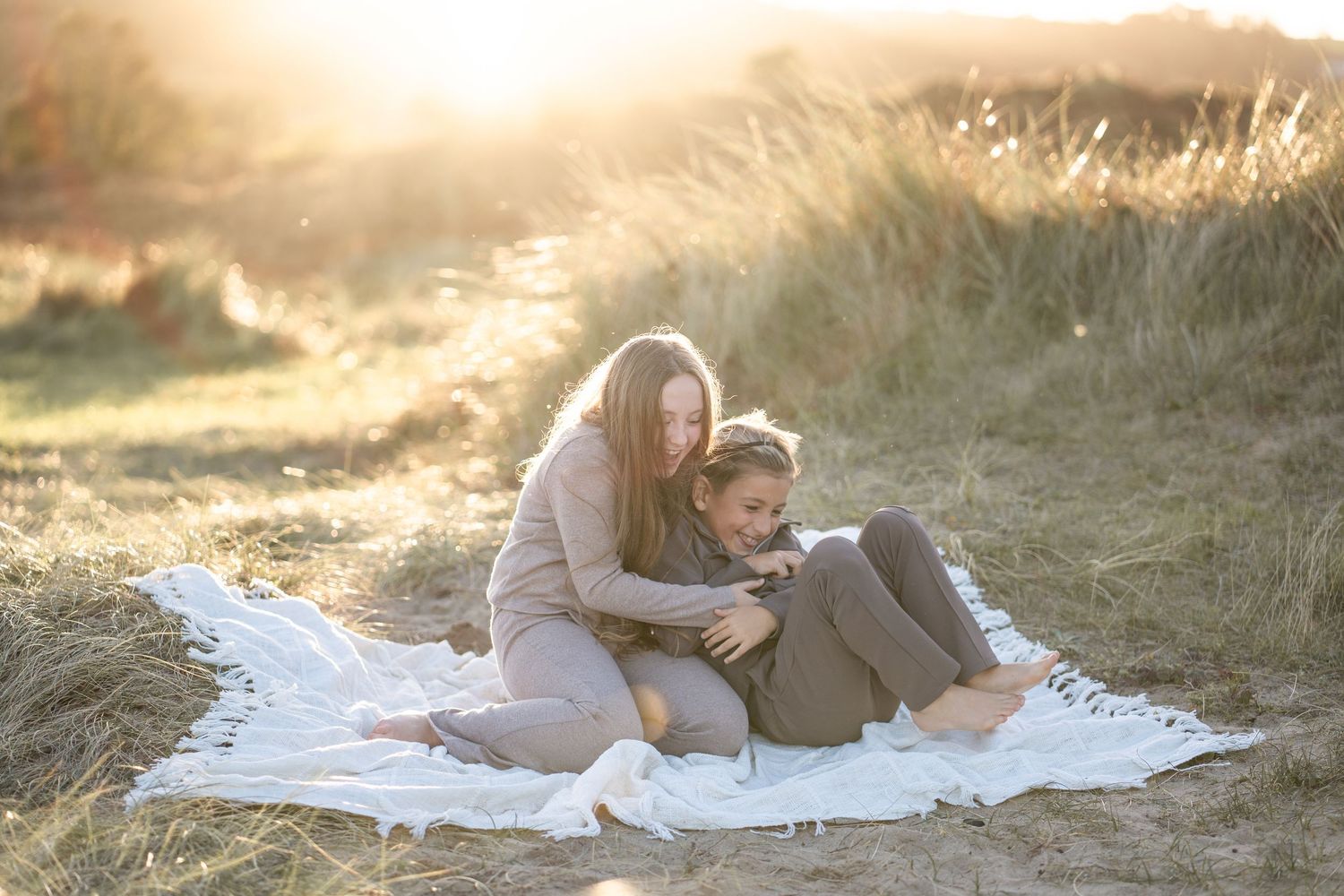 Romantic couple lying on white blanket in sunlit meadow during golden hour sunset photography session.