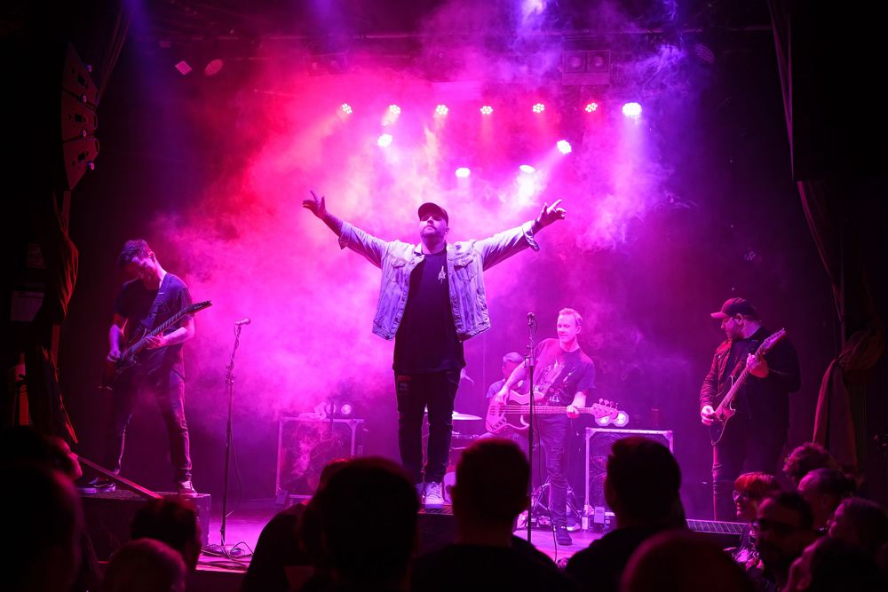 Concert stage lit with vibrant purple and pink lights during an energetic live music performance.
