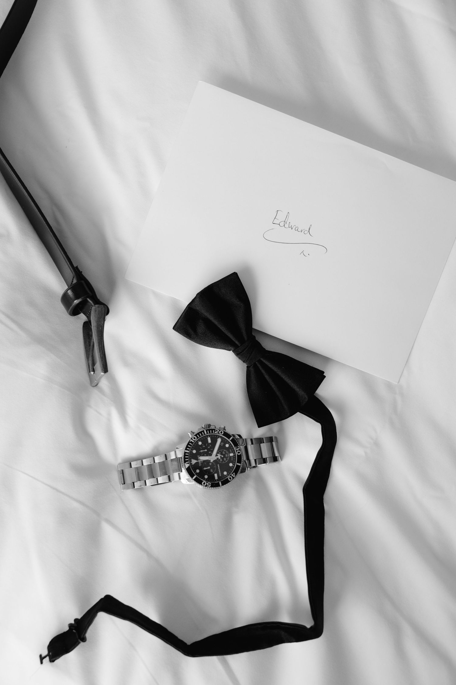 A silver wristwatch with black bow tie accessories arranged on a white background in a minimalist style.