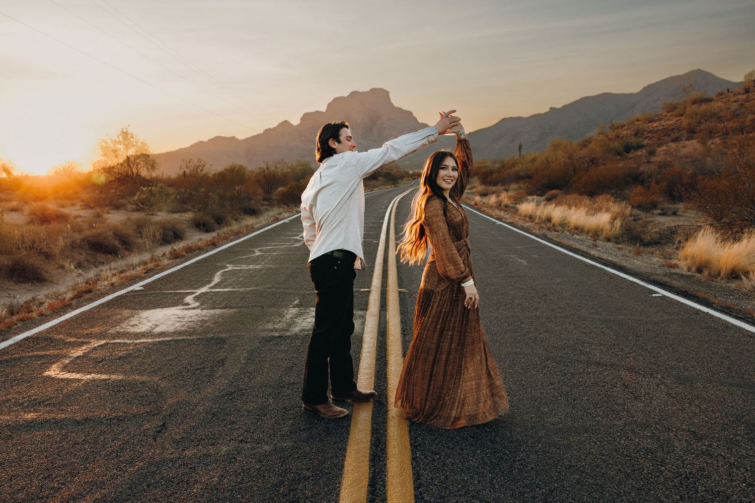 A couple stands on an empty desert road at sunset with mountains in the background near the Salt River.