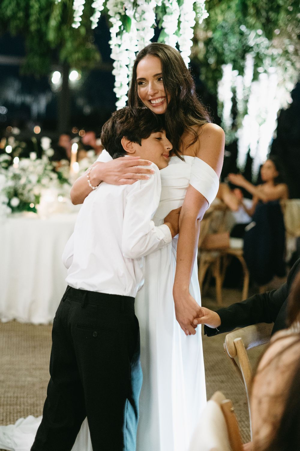 Two people in black and white formal attire embrace while dancing at an elegant indoor event with hanging floral decor.