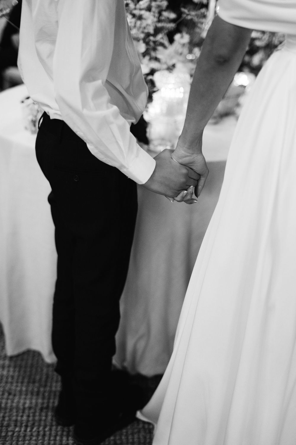Black and white wedding photo showing close-up of bride and groom's formal attire as they stand together.